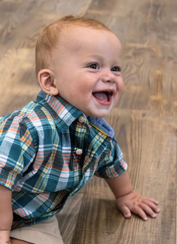 Baby boy smiling in plaid shirt.