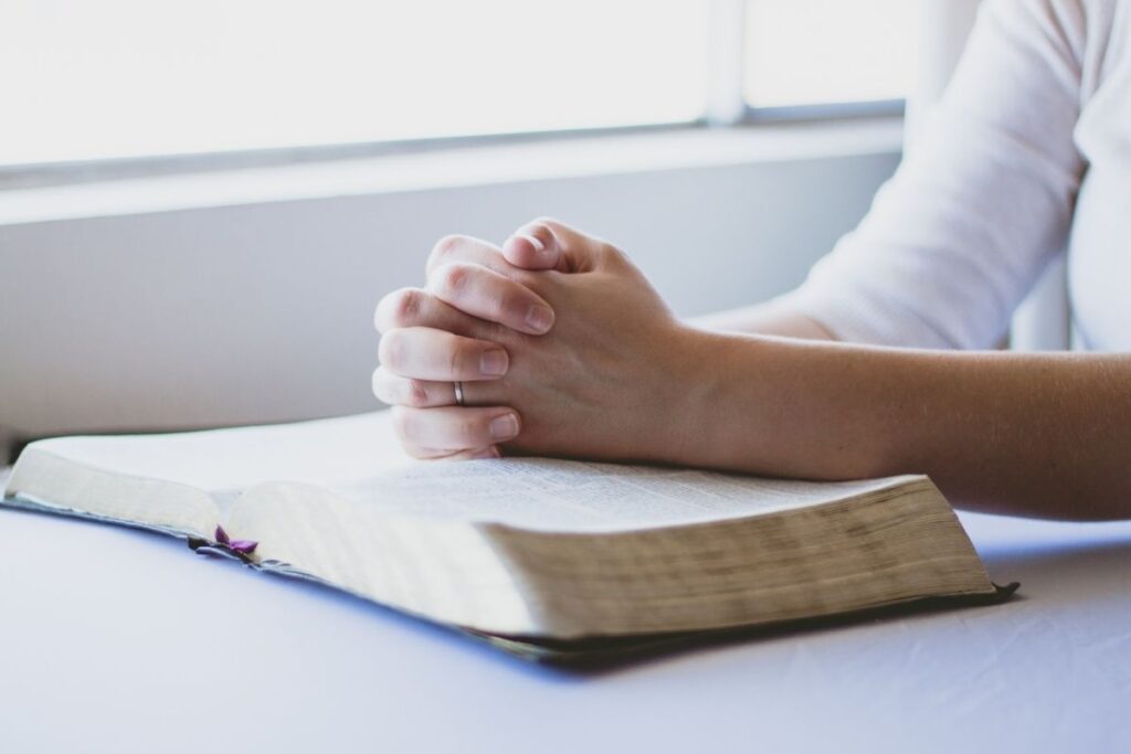 Hands folded in prayer over a Bible