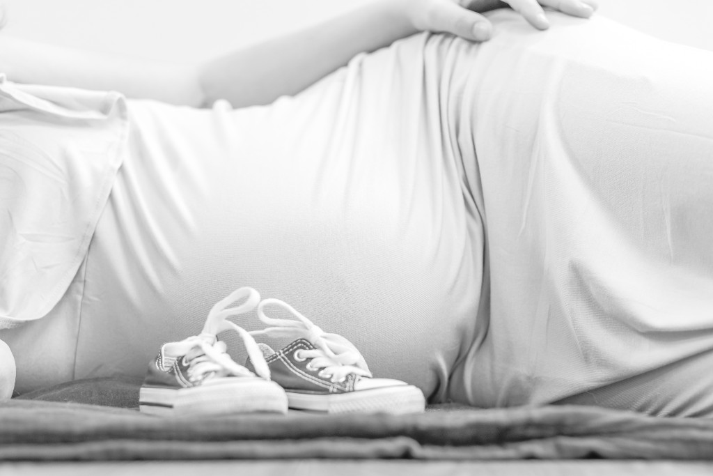 Expecting mom laying on her side with baby shoes sitting beside her.
